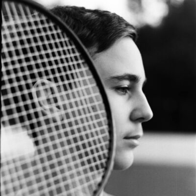 Side view of black and white young male tennis player standing on court with racket and looking away